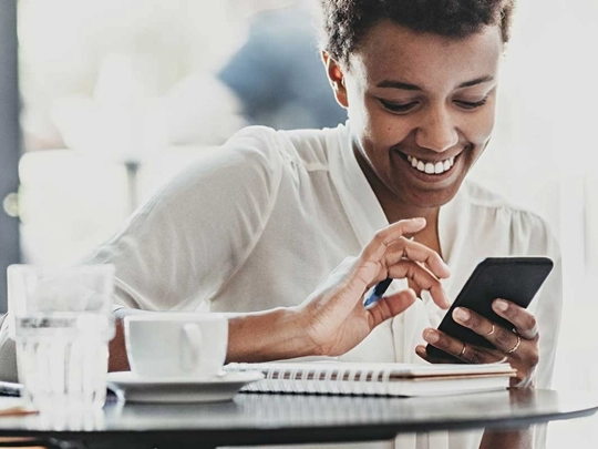 Mujer sonriendo mientras sostiene un celular y bebe café