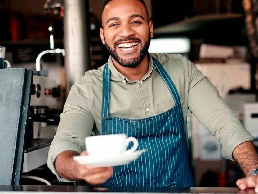 Un barista sonriente entregándote una taza de café en la cafetería