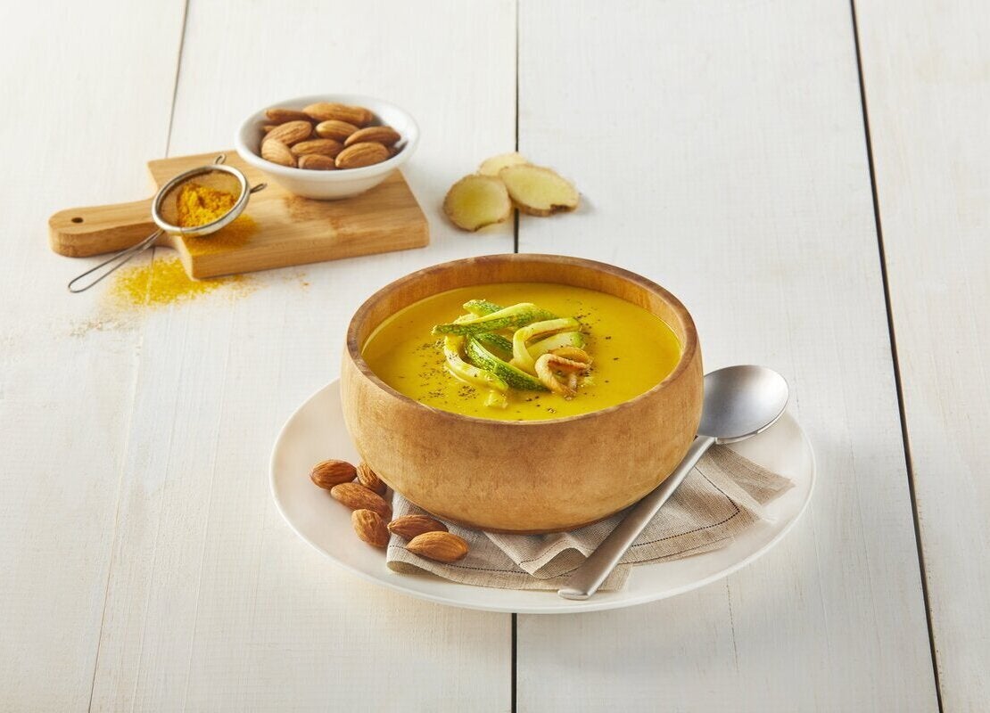 Crema de vegetales sin lactosa servida a la mesa y al lado una tabla de cortar con los ingredientes