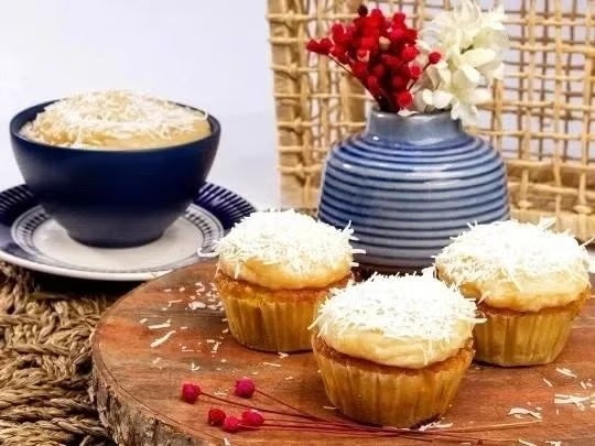 Tres cupcakes y un bizcocho servidos sobre una mesa de madera decorada con un florero azul