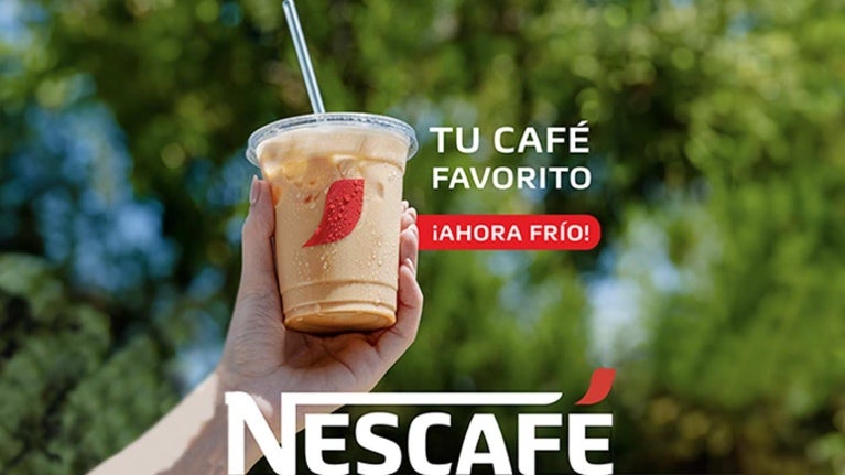 Mano de una mujer sostiene hacia lo alto un vaso de café frío NESCAFÉ® que incluye una pajilla