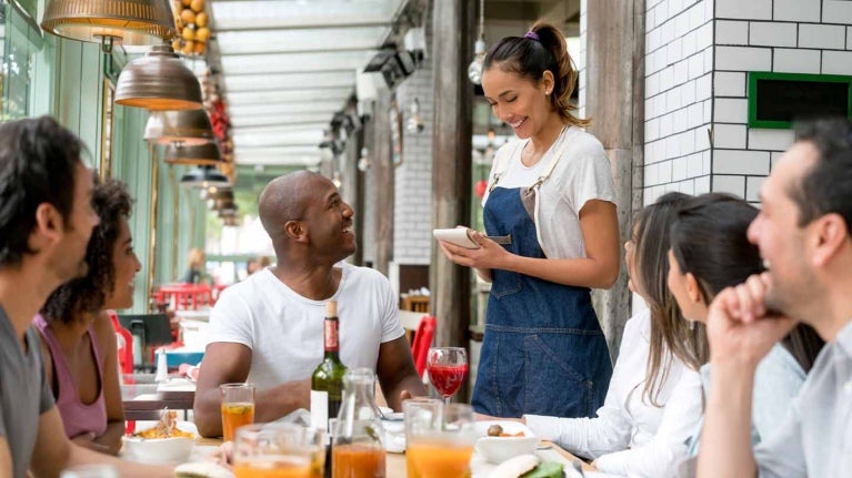 Mesera toma la orden de un grupo de comensales que están en una mesa en un negocio de food service