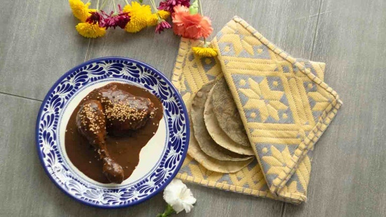 Plato con dos piezas de pollo cubiertas de la salsa mole, al lado 4 tortillas de maíz en un mantel