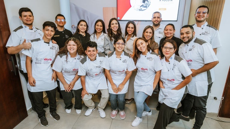 Grupo de jóvenes con mandiles blancos sonríen para la cámara, celebrando el lanzamiento del programa YOCUTA 2.0 de NESTLÉ®