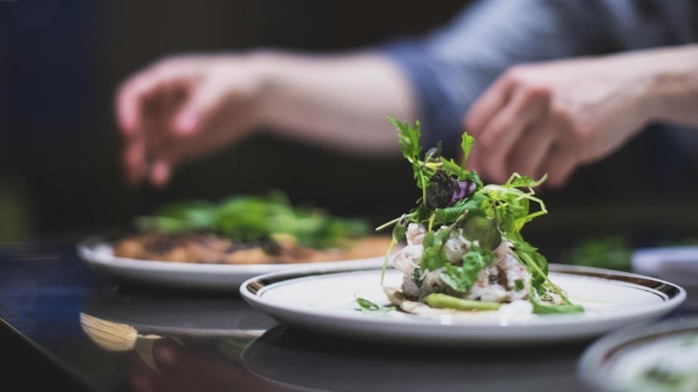 Manos de chef decora dos platillos sobre una mesa, que hacen parte de las food trends 