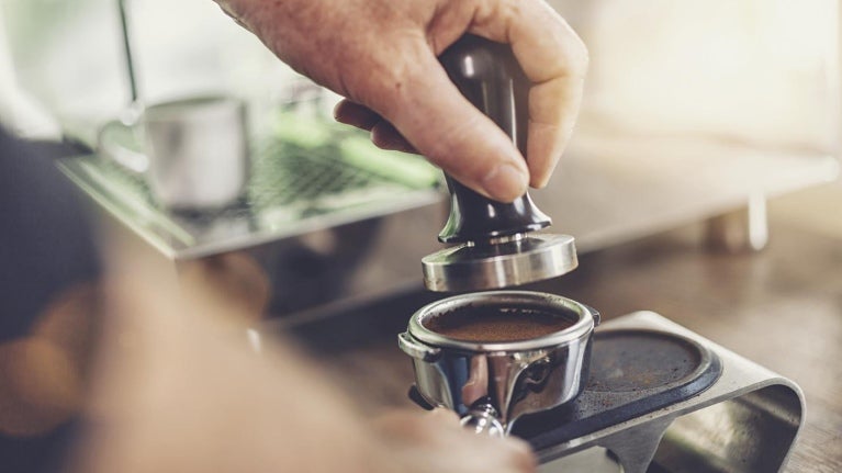 Mano de un barista utiliza herramientas como un tamper y un apisonador para café