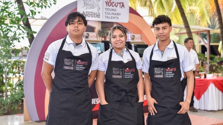 Tres jóvenes con delantales posan juntos, representando el programa YOCUTA de Nestlé