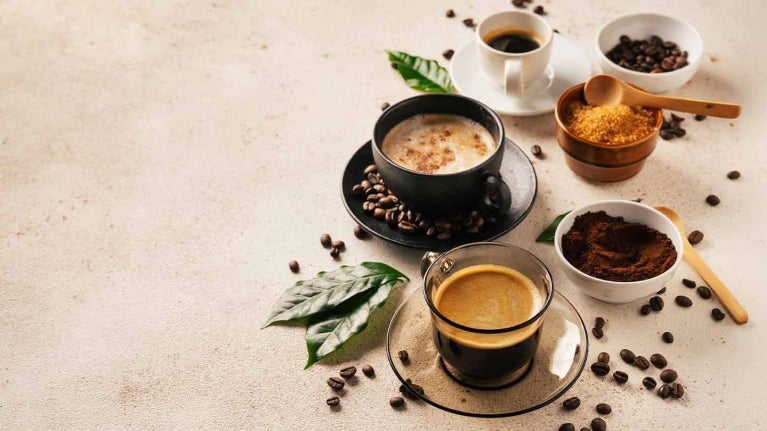 3 diferentes bebidas y productos de café junto con hojas y granos en una mesa