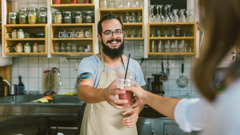 Barista entrega un smoothie, una de las bebidas para cafetería, a una clienta