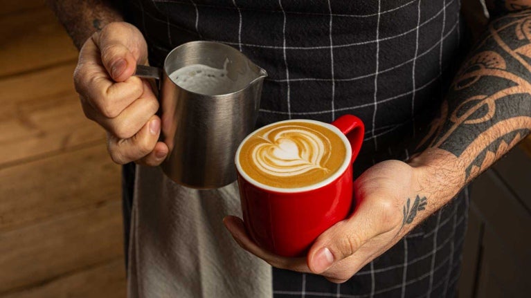 Manos de barista sostienen una taza de café recién preparada con una técnica de latte art