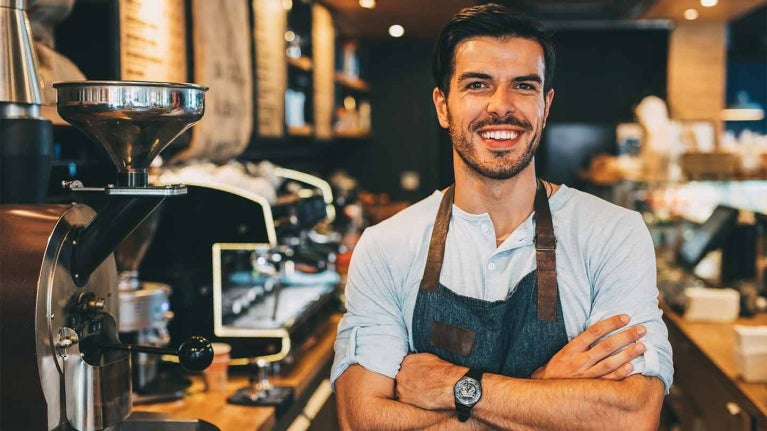 Dueño de un negocio de café-bar sonriendo con los brazos cruzados