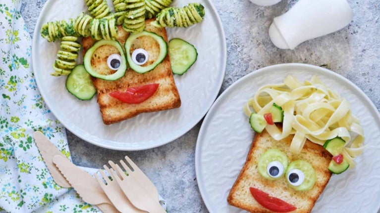 Sobre una mesa, dos platos con pan, pasta y verduras formado una cara feliz para un menú infantil