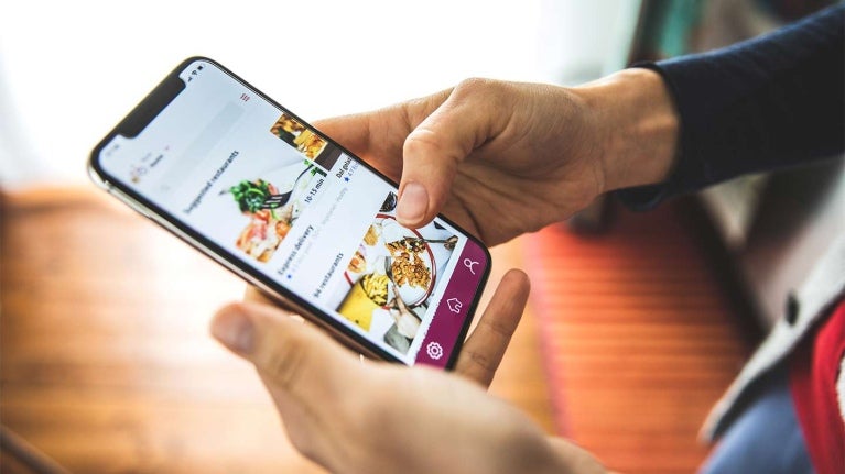 Manos sostienen un celular que muestra una plataforma de entrega a domicilio con diferentes platillos