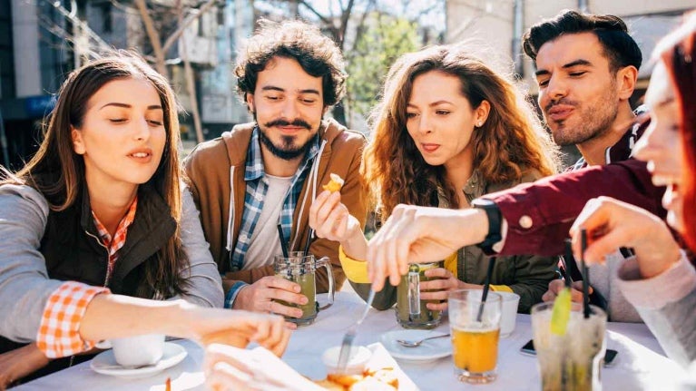 Grupo de comensales sentados en una mesa al aire libre toman aperitivos y bebidas