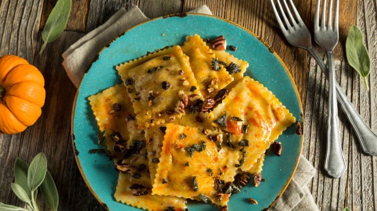 Raviolis de calabaza con salsa de frutos secos y ajedrea en un plato azul y alrededor sus ingredientes