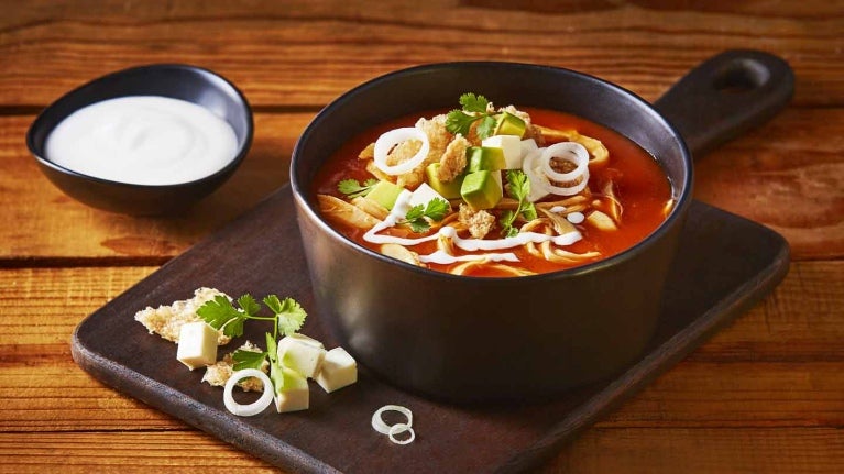 Sopa de pollo con verduras servida sobre una tabla y acompañada con crema de leche