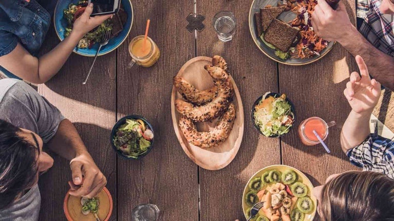 4 amigos consumen platillos sin carne mientras platican en una mesa al aire libre