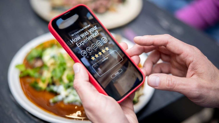 Manos de hombre sostienen un smartphone donde califica su experiencia en un restaurante frente a un platillo