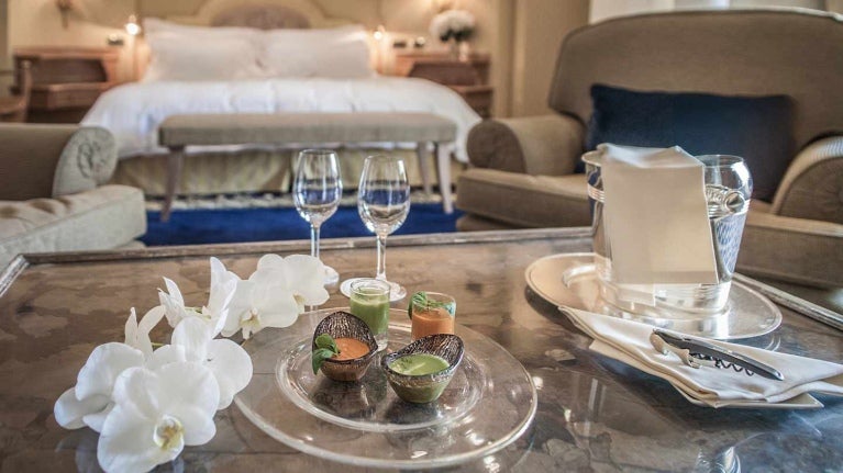 Mesa con copas, velas, decoración y al fondo una cama, mesitas y sillón en una habitación de hotel