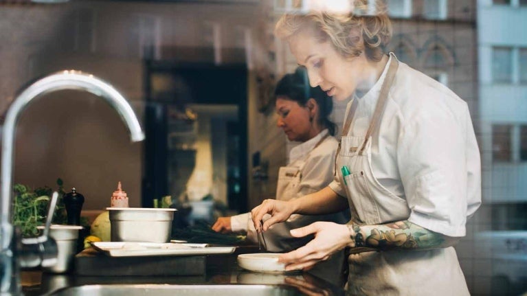 Dos chefs lavan y seleccionan ingredientes en el mesón de una cocina comercial