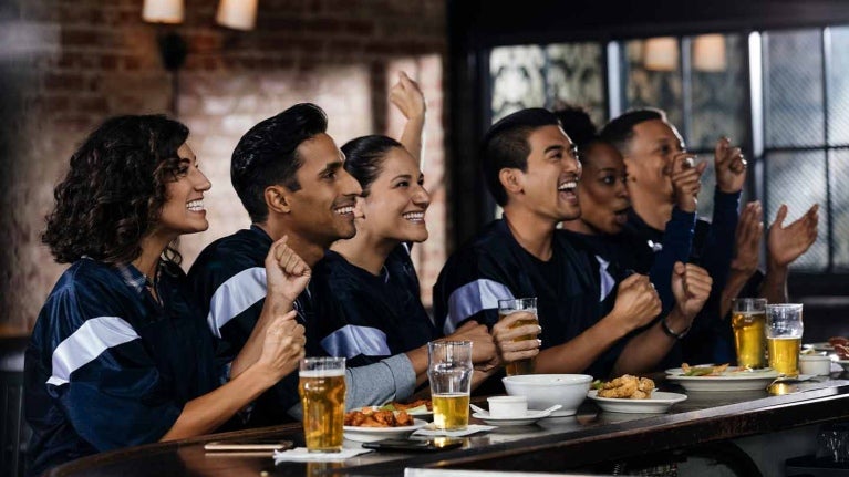 Grupo de amigos festejan sentados en la barra de un gastrobar donde hay comida y bebidas