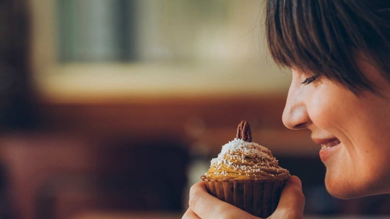 Mujer sostiene frente a su rostro un cupcake de frutos secos mientras disfruta su aroma