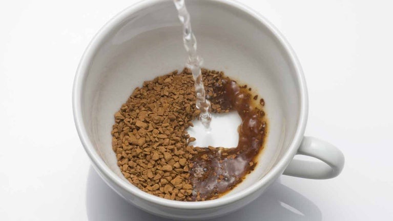 Taza de porcelana blanca con café soluble sobre el que se vierte agua caliente para preparar la bebida