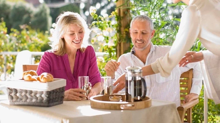 Mesera sirve café en greca francesa a una pareja sentada a la mesa de un hotel al aire libre