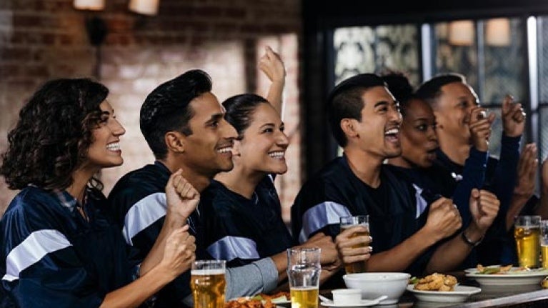 Grupo de amigos festejan sentados en la barra de un gastrobar donde hay comida y bebidas