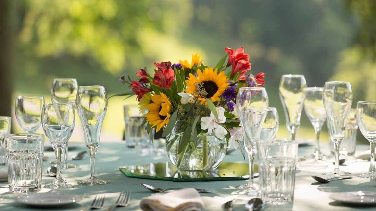 Mesa redonda al aire libre puesta para una comida formal con copas de cristal y flores en el centro