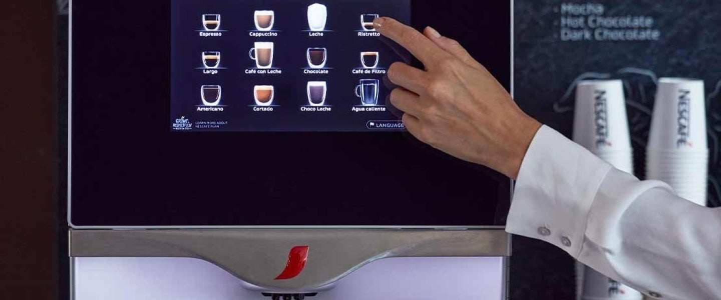 La mano de una persona eligiendo la bebida a preparar desde la pantalla táctil de una máquina NESCAFÉ.
