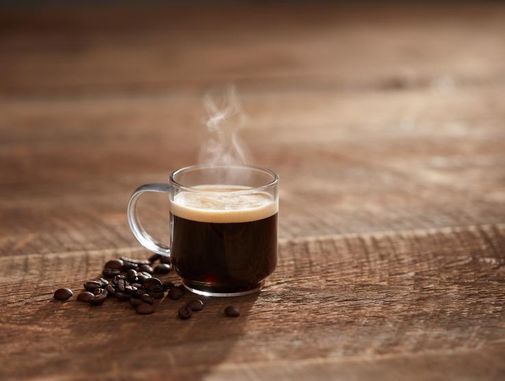 taza de vidrio con café Espresso y granos de café sobre tabla de madera