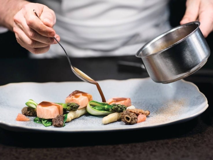 Manos de chef agregando salsa sobre un platillo con una cuchara
