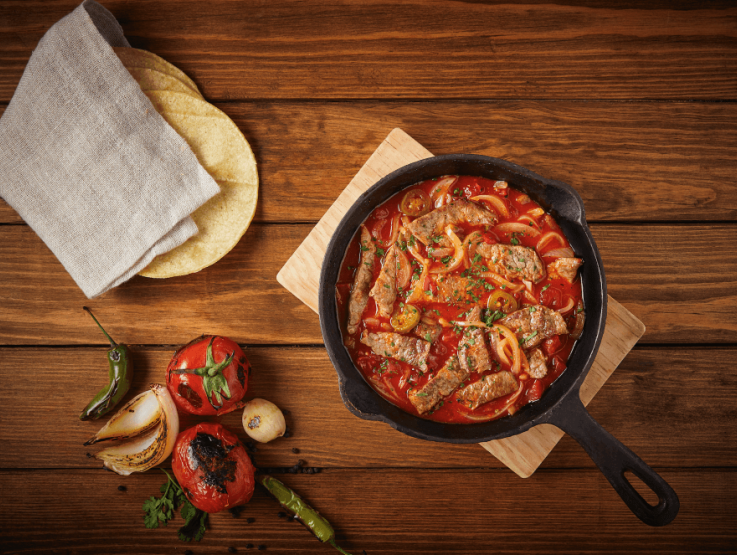 Estofado en sartén de hierro fundido junto a verduras rostizadas y tortillas de maíz