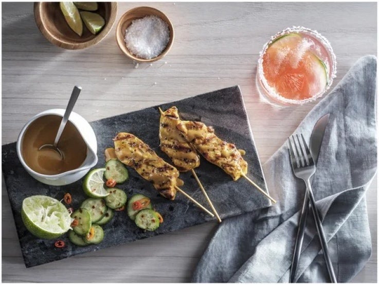 Brochetas y vegetales asados y un recipiente con salsa MINOR'S® sobre una tabla, al lado una bebida fría