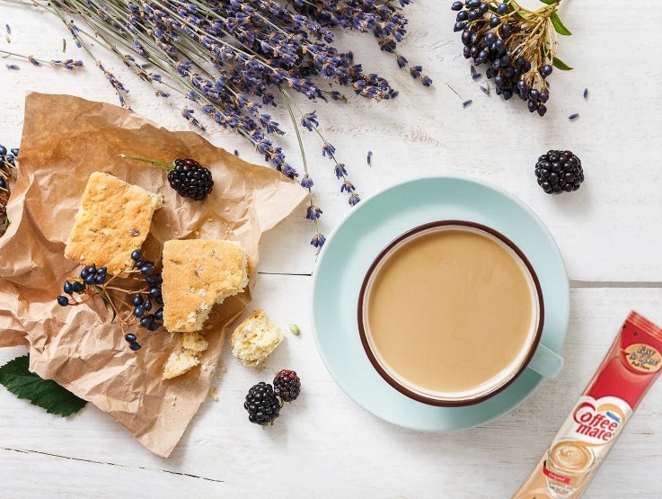 Taza azul de café elaborada con NESCAFÉ® y COFFE MATE®, al lado un stick del producto, galletas y bayas