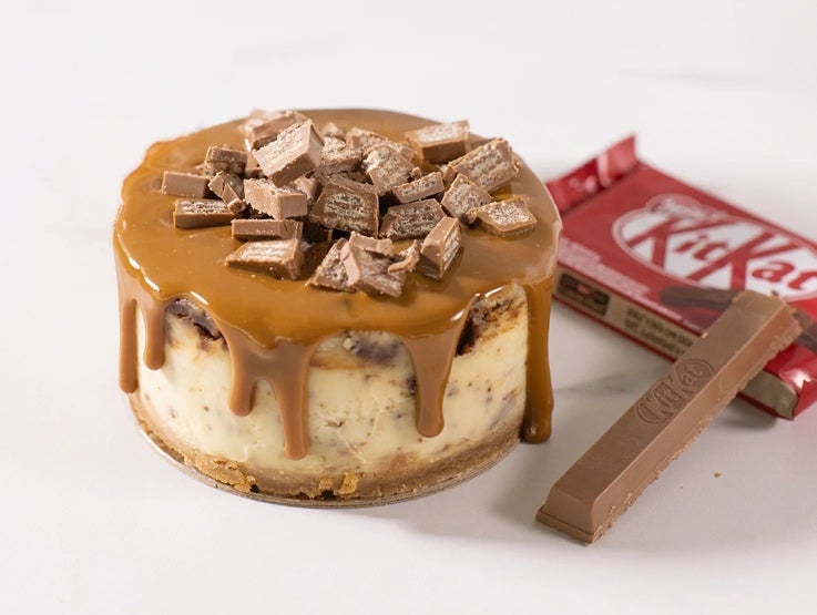 Cheesecake decorado con dulce de leche y trozos de KITKAT® 4 Fingers, al lado, empaque del producto