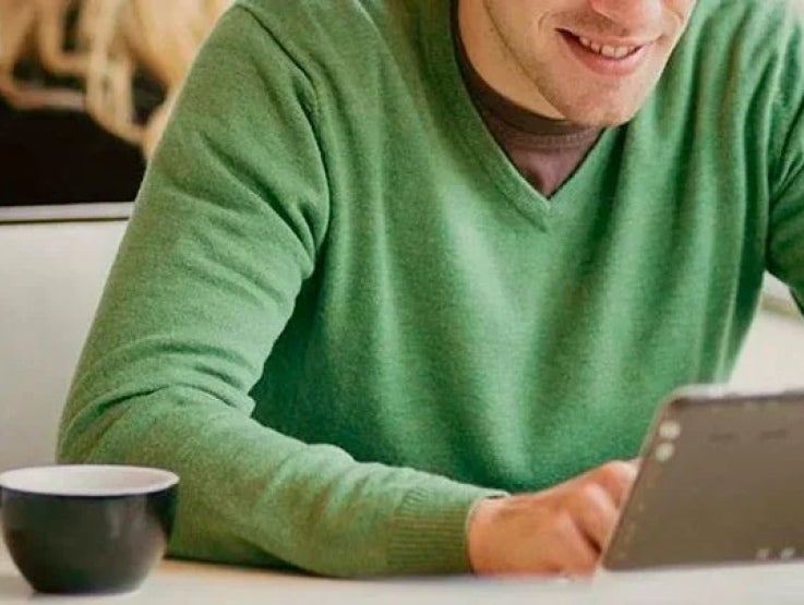 Hombre revisa su tablet mientras está sentado a la mesa sobre la que hay una taza negra de porcelana
