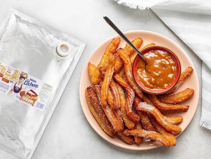 Plato de churros y recipiente pequeño con dulce de leche junto a una bolsa de LA LECHERA®