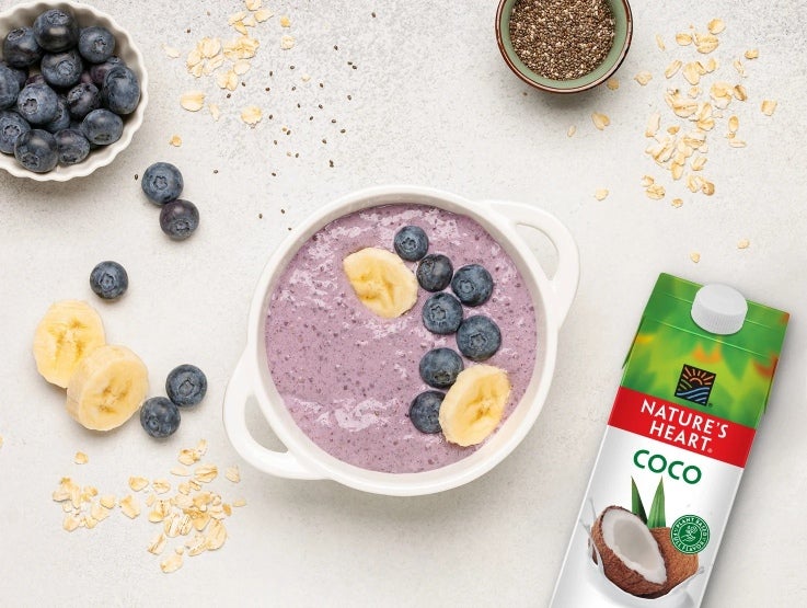 Taza de yogurt con arándanos y rodajas de banano, al lado una Bebida de Coco NATURE'S HEART®