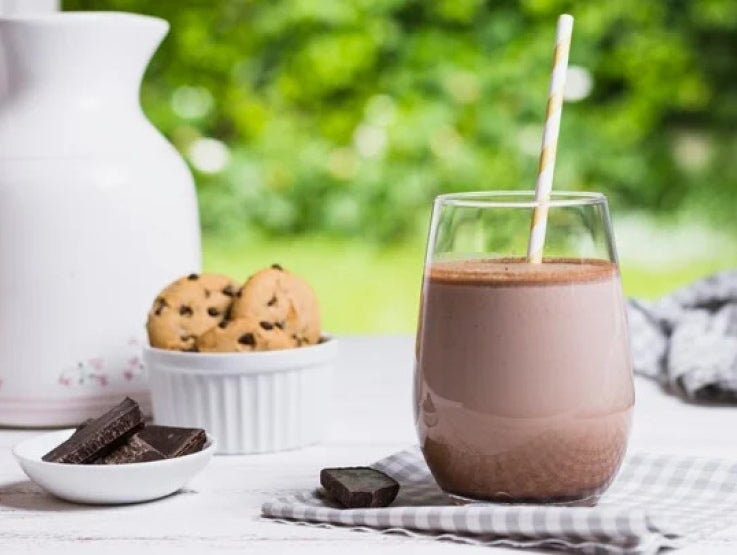 Vaso de bebida elaborada con NESQUIK®, alrededor galletas y trozos de chocolate en tazas sobre una mesa