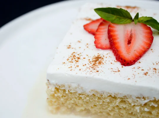 Postre de tres leches de vainilla decorado con chantilly y láminas de fresa 