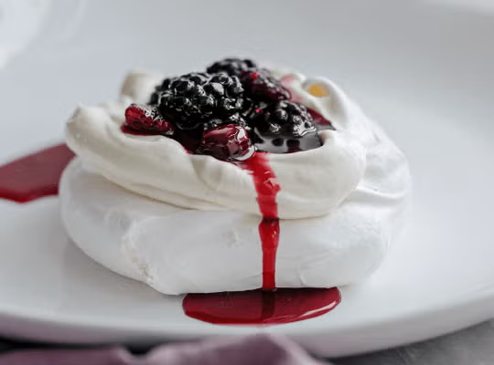 Servido en un plato, Pavlova con Crema Chantilly y Salsa de Berries