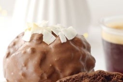 Muffin con KITKAT® cubierto de chocolate y decorado con virutas de coco, acompañado de una taza de café